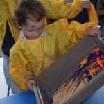 boy titling a container with lots of colours of paint inside