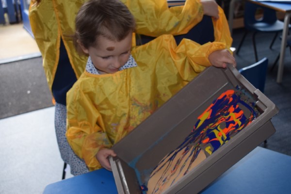 boy titling a container with lots of colours of paint inside