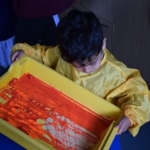 young boy adding paint to a yellow container